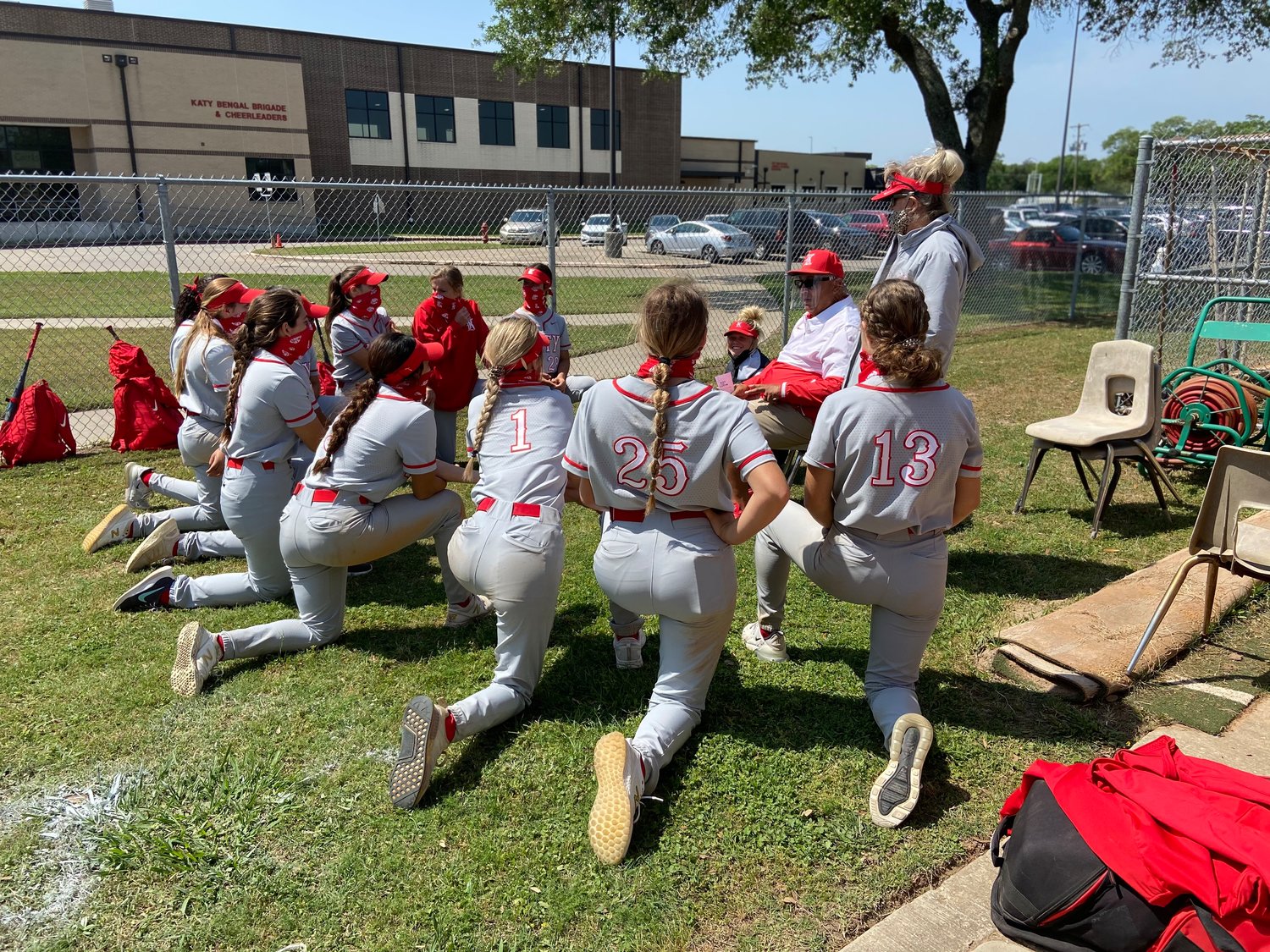 Katy High softball coach Kalum Haack, sitting in the middle, talks to his team Saturday, April 10, after its 9-0 win over Taylor that secured the program’s sixth straight outright district championship.